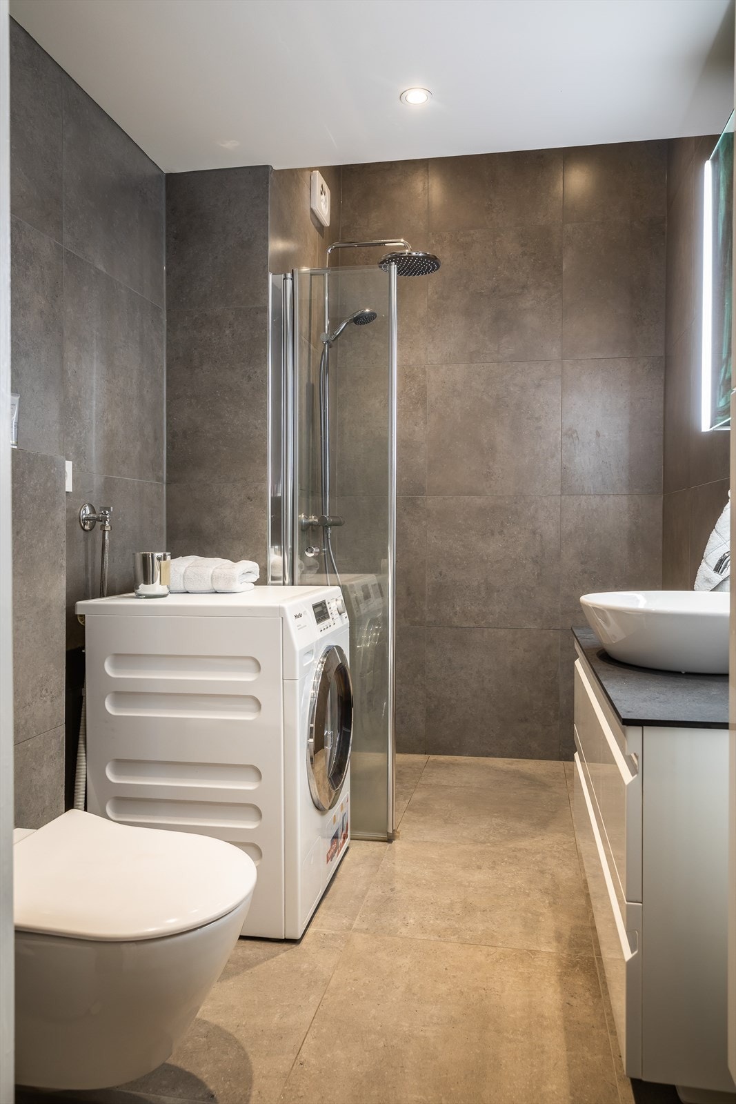 Dusj på gulv, servant, veggfestet klosett med innebygget sisterne og opplegg for vaskemaskin. Galleribilde