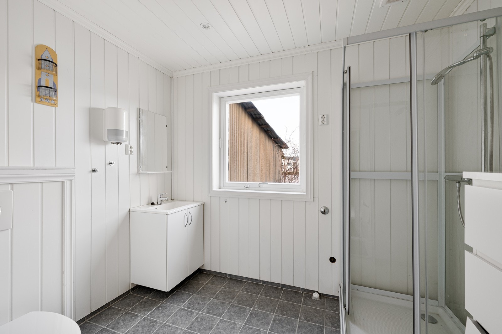 Bad med flislagt gulv. Innredet med servant i baderomsskap, speil, toalett og dusjkabinett. Galleribilde