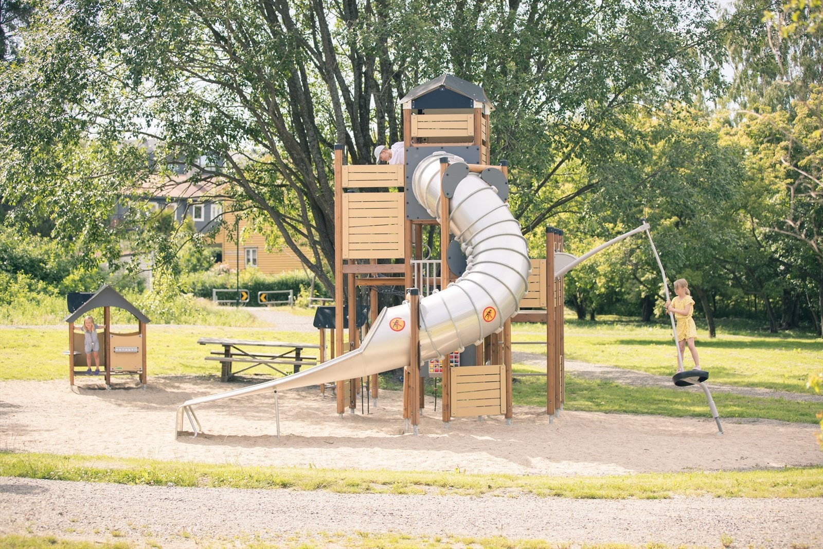 Jungelen like ved er en spennende lekeplass for barna hvor det er masse boltreplass med klatreapparater, grønt gress og vakre trær Galleribilde