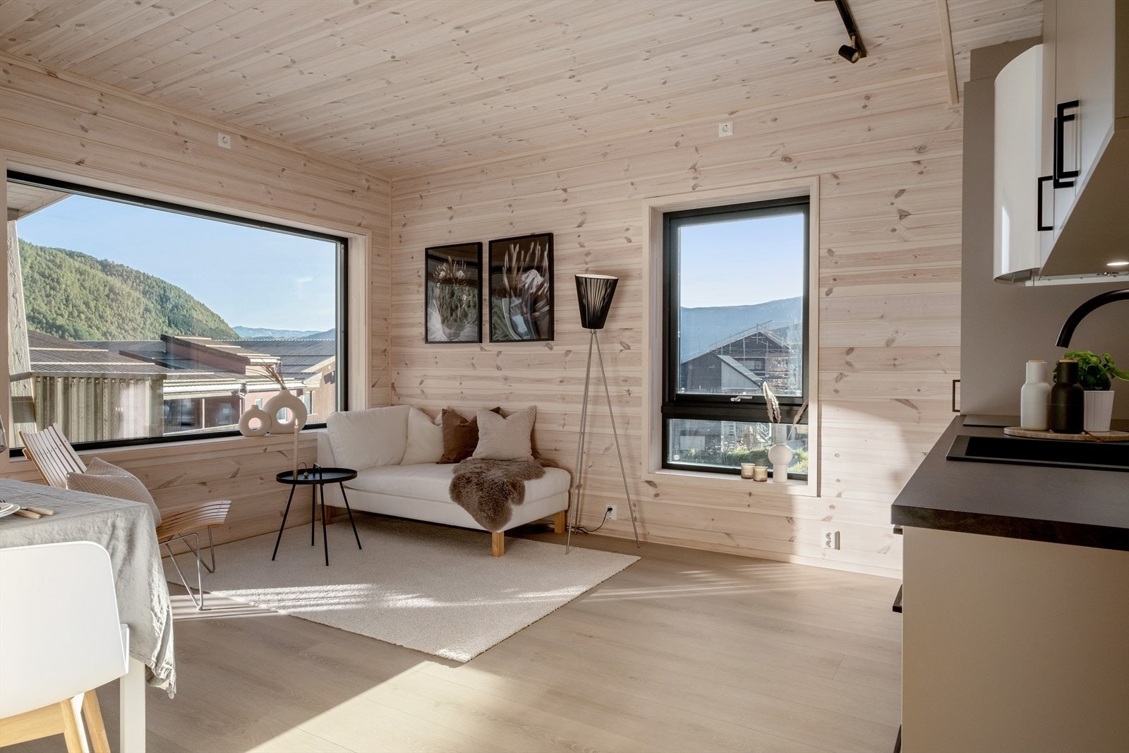 Åpen stue/kjøkkenløsning med store vindusflater, lekker en-stavs høytrykkslaminatgulv og panelkledning som rammer inn hele rommet. Galleribilde