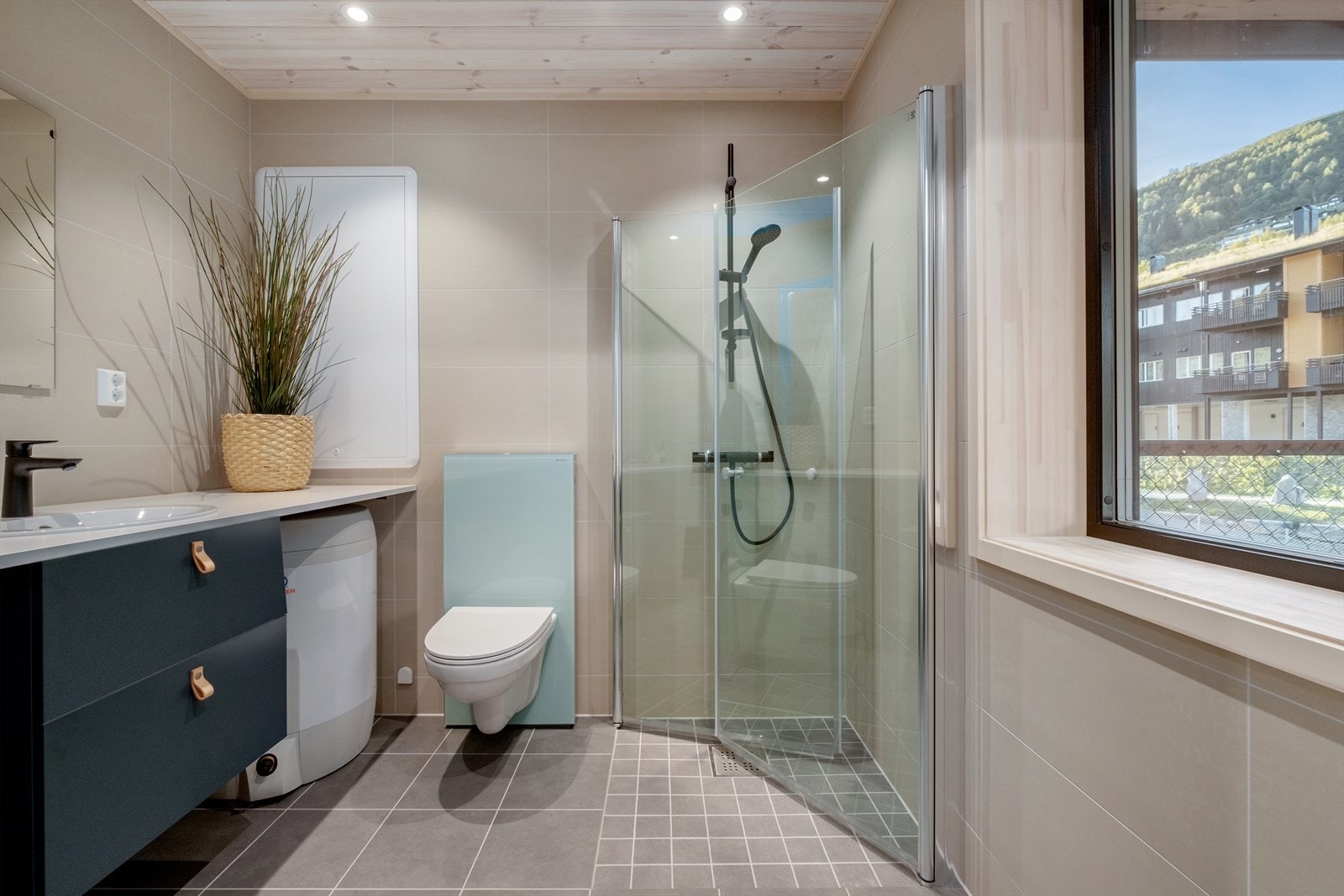 Badet inneholder vegghengt wc, dusj med dusjdører, vegg til vegg benkeplate, baderomsinnredning, speil, servant, varmtvannsbereder og opplegg til vaskemaskin. Galleribilde