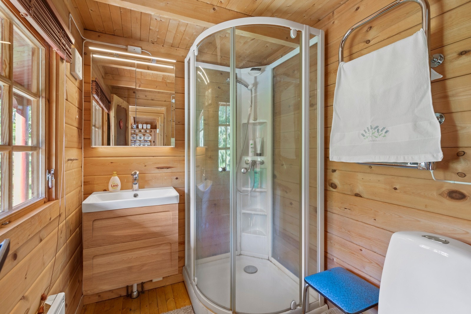 Badet har furubord på gulv og tømmervegger. Rommet er utstyrt med dusjkabinett med direkte kobling til avløp, toalett, elektrisk avtrekksvifte og baderomsinnredning med servant og speilskap. Galleribilde