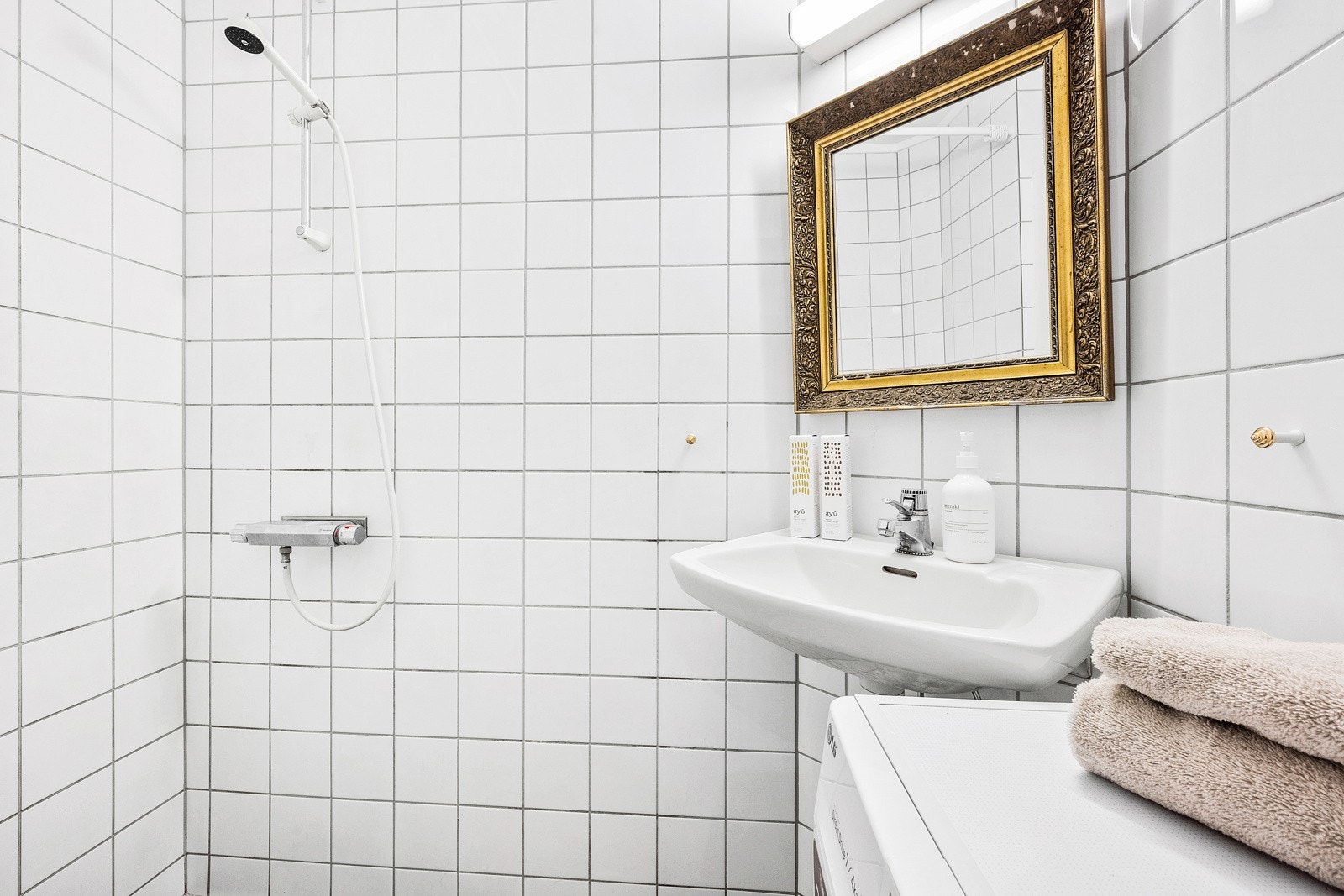 Bad med flislagte overflater og varme i gulvet. Innredningen består av servant, dusj og opplegg for vaskemaskin. Galleribilde