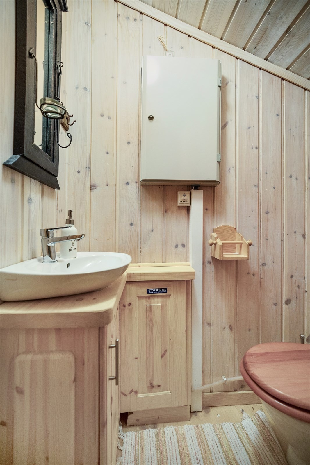 Toalett og vask. Sikringsskapet er plassert på vegg. Tregulv og panel på vegg/tak Galleribilde