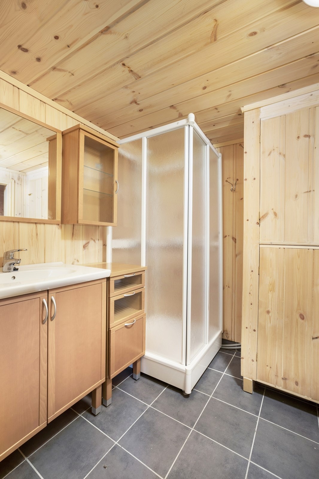 Badet i første etasje er innredet med dusjkabinett og servantskap. Flis på gulvet med varmekabler og panel på vegg/tak. Galleribilde