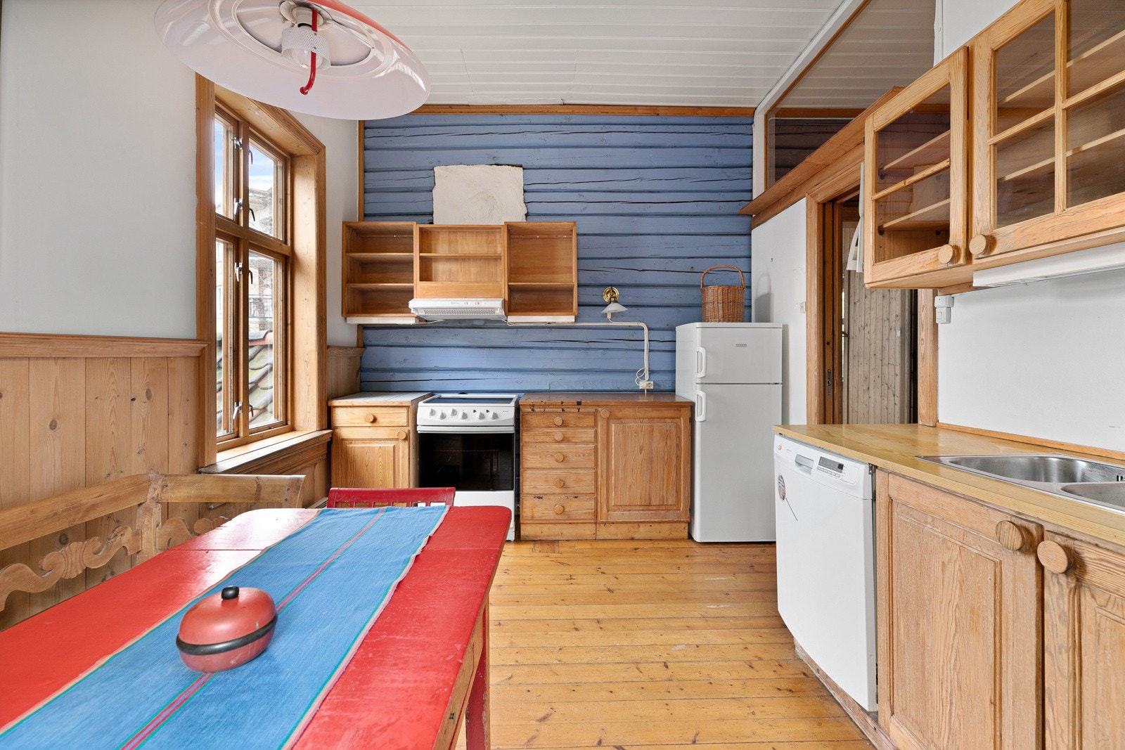 Overflatene i rommet består av originale tregulv, hvitmalte veggflater, noe brystningspanel og en nydelig tømmervegg, fremhevet i blått. Galleribilde