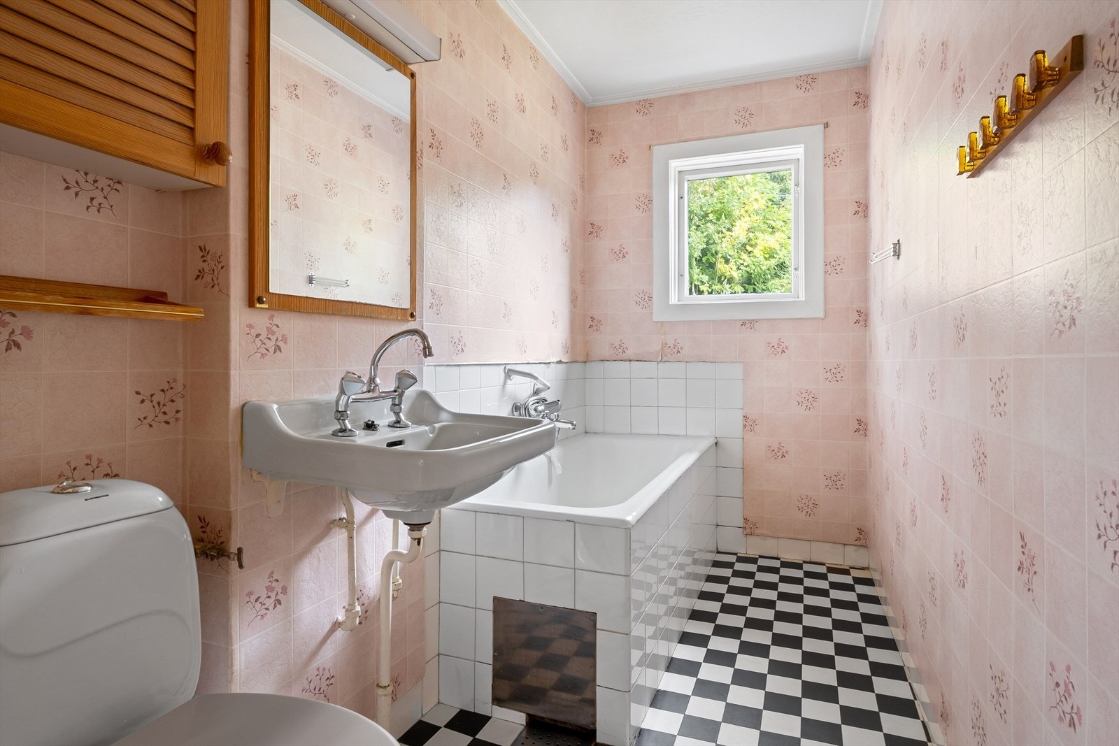 Eldre bad/ WC med fliser på gulv, tapet på veggen og malt himling. Rommet inneholder WC, badekar og servant. Galleribilde