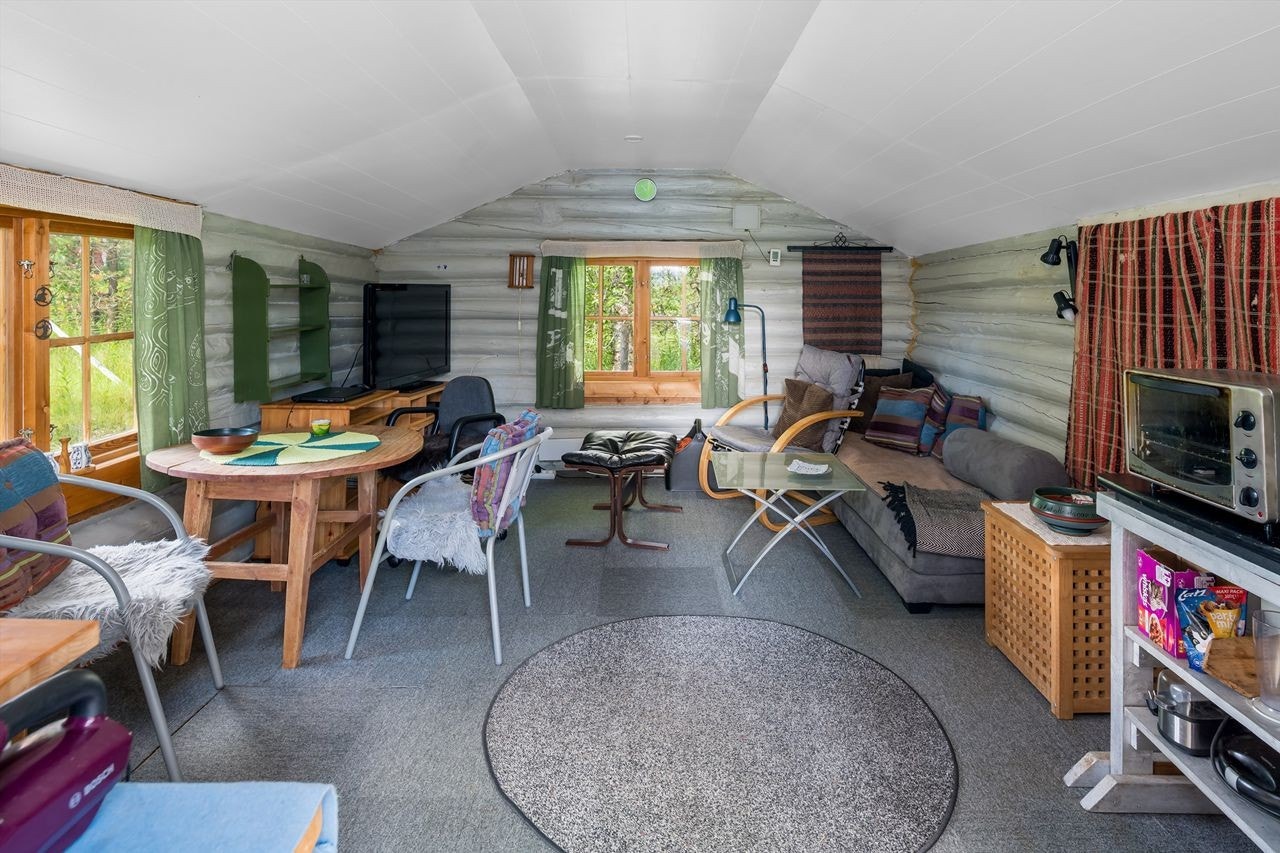 Hovedhytta er en tømmerstue med koselige malte tømmervegger. Her er plass til sofa, spisebord og kjøkkenkrok Galleribilde