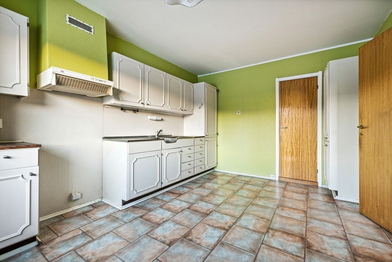 Kjøkkeninnredning har melaminbelagte skrog, respatex benkeplater og benkeplate av stål med nedfelt dobbel oppvaskkum Galleribilde