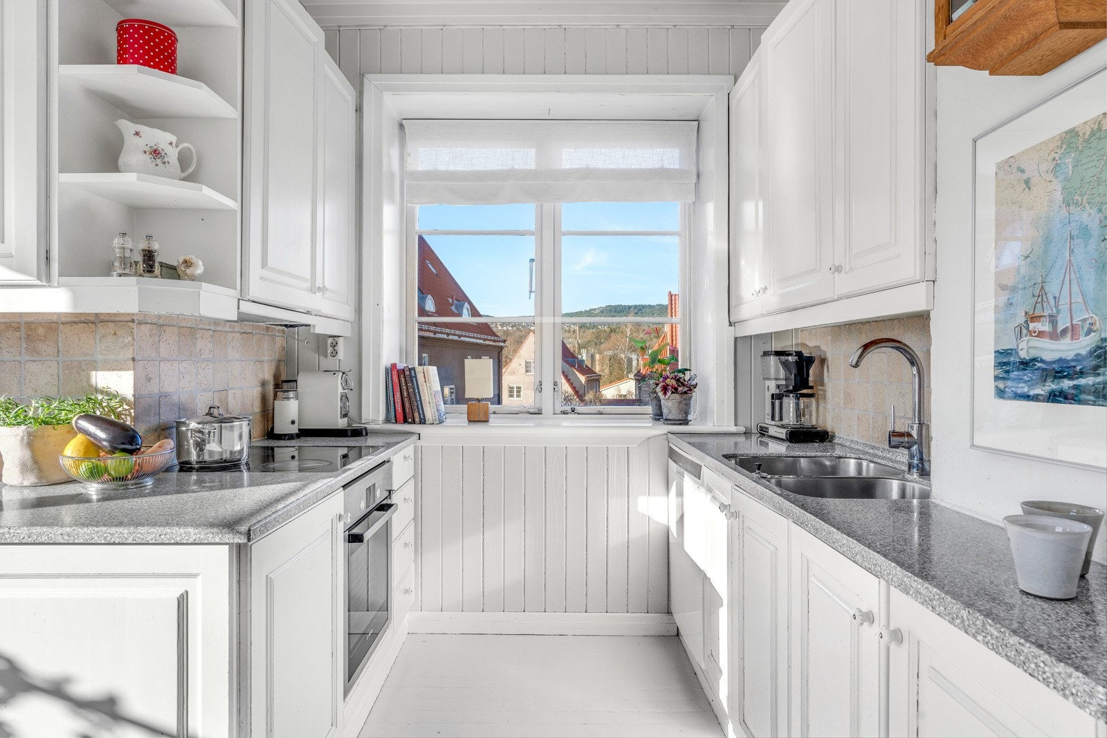 Hvitmalt innredning av profilert heltre med fliser over benk, Corian benkeplate og integrert komfyr. Galleribilde