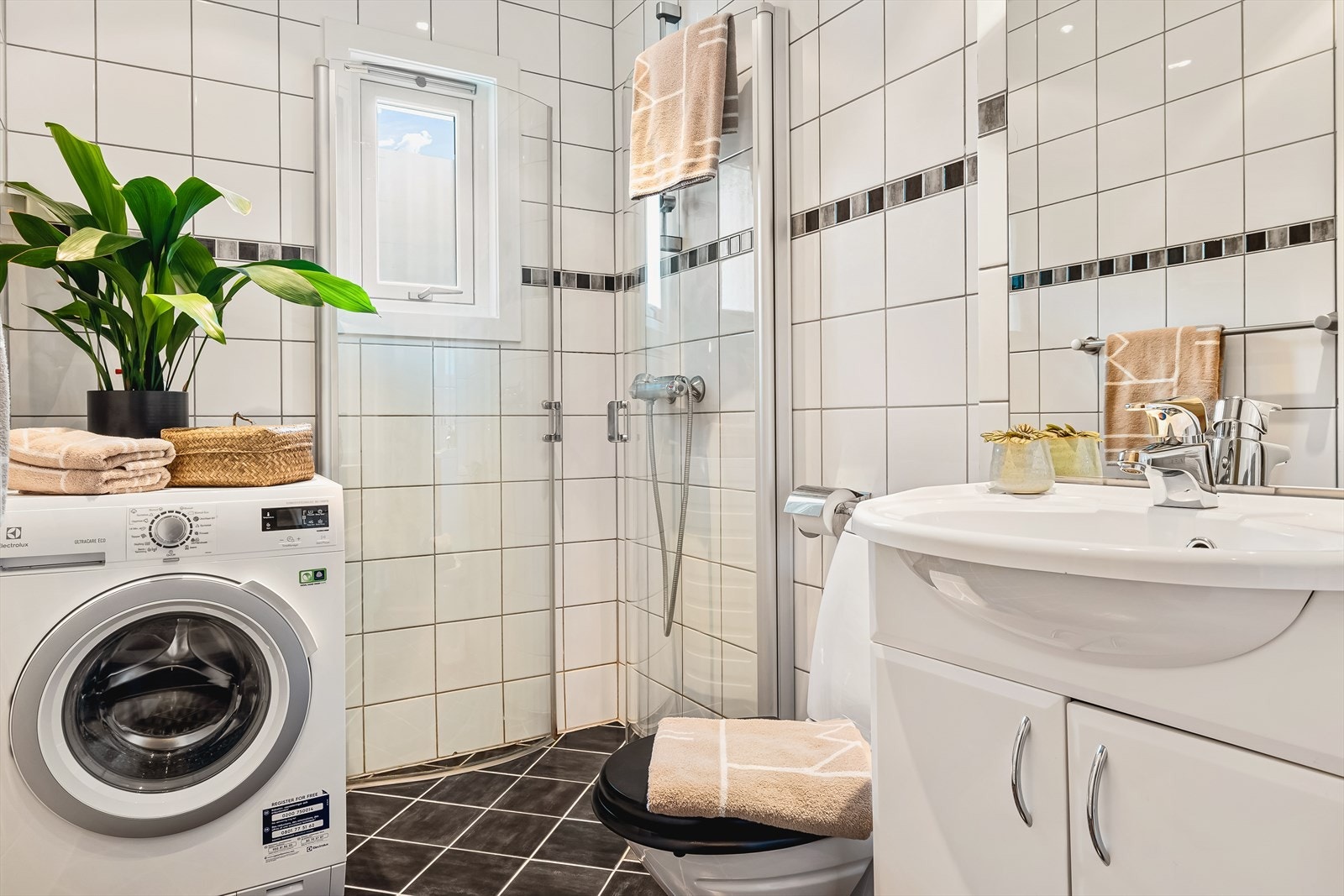 Badet er lekkert innredet med keramiske fliser på gulv og vegger. Tidløs innredning med heldekkende servant, toalett, buede dusjdører i glass, samt speil med belysning over. Galleribilde