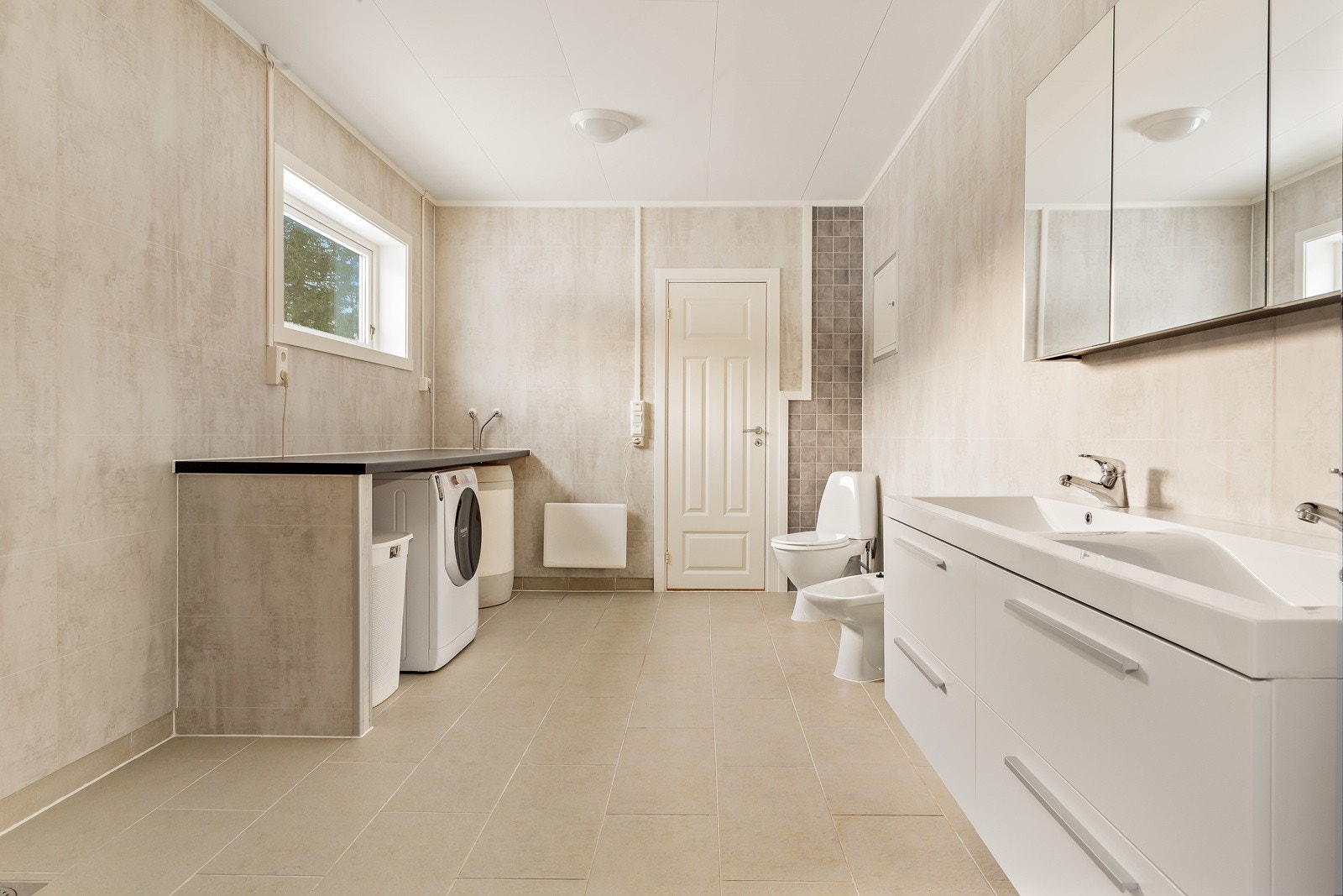 Vegg i vegg med baren finner du et stort bad/vaskerom. Baderomsinnredningen er i laminat utførelse med speilfronter på overskapene. Det er montert 116 l. varmtvannsbereder. I 2. etg. er det montert 200 l. varmtvannsbereder på bod. Galleribilde