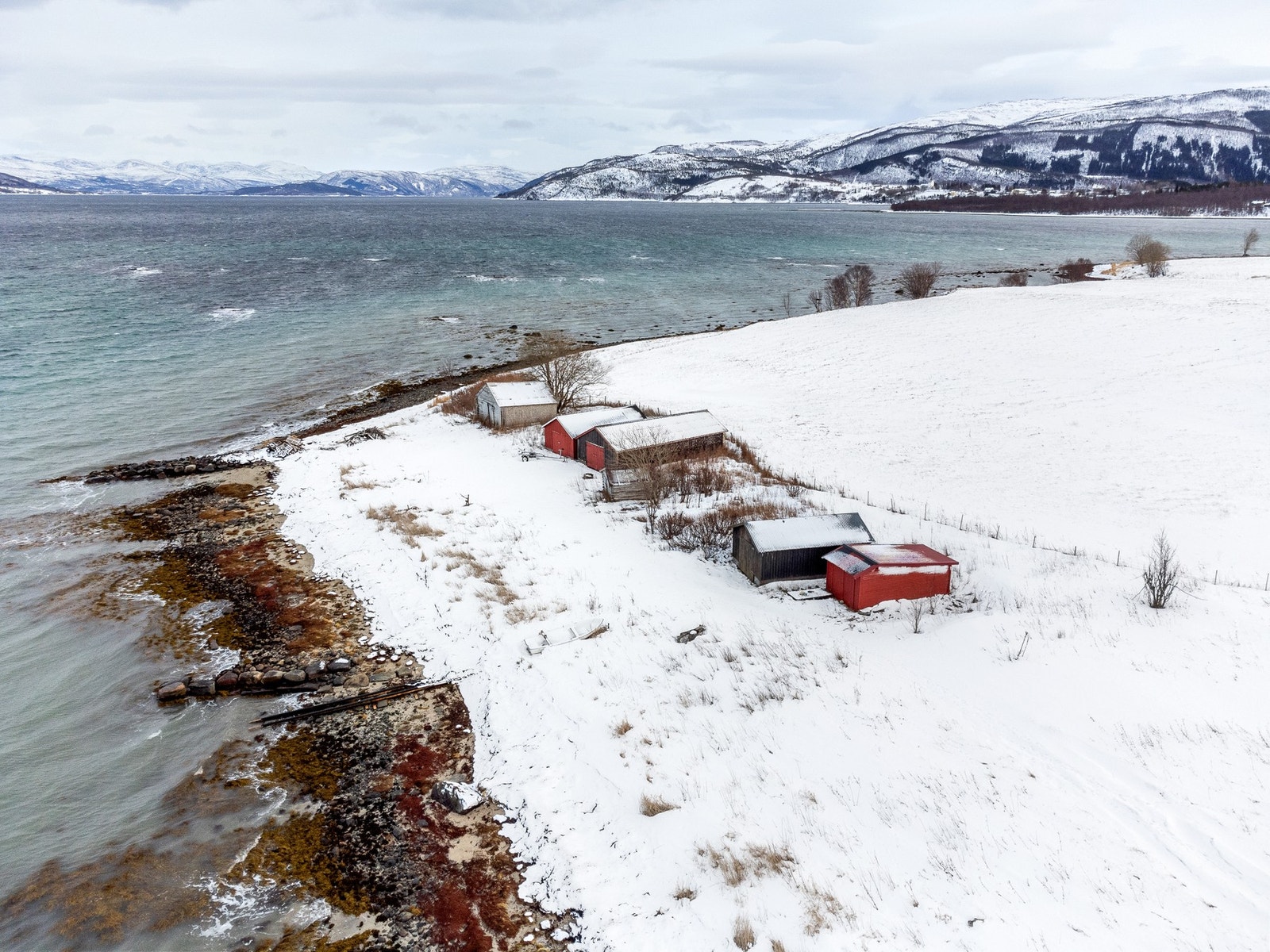 Bilde av naustene langs fjæra. Et av disse tilhører boligen. Galleribilde