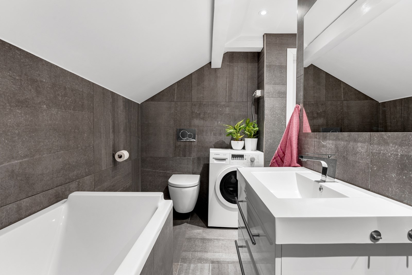 Ellers har badet veggmontert wc og servant over innredning med skuffer. Det er fliser med varme på gulv som sørger for en lun og god temperatur og det er downlights i himling Galleribilde