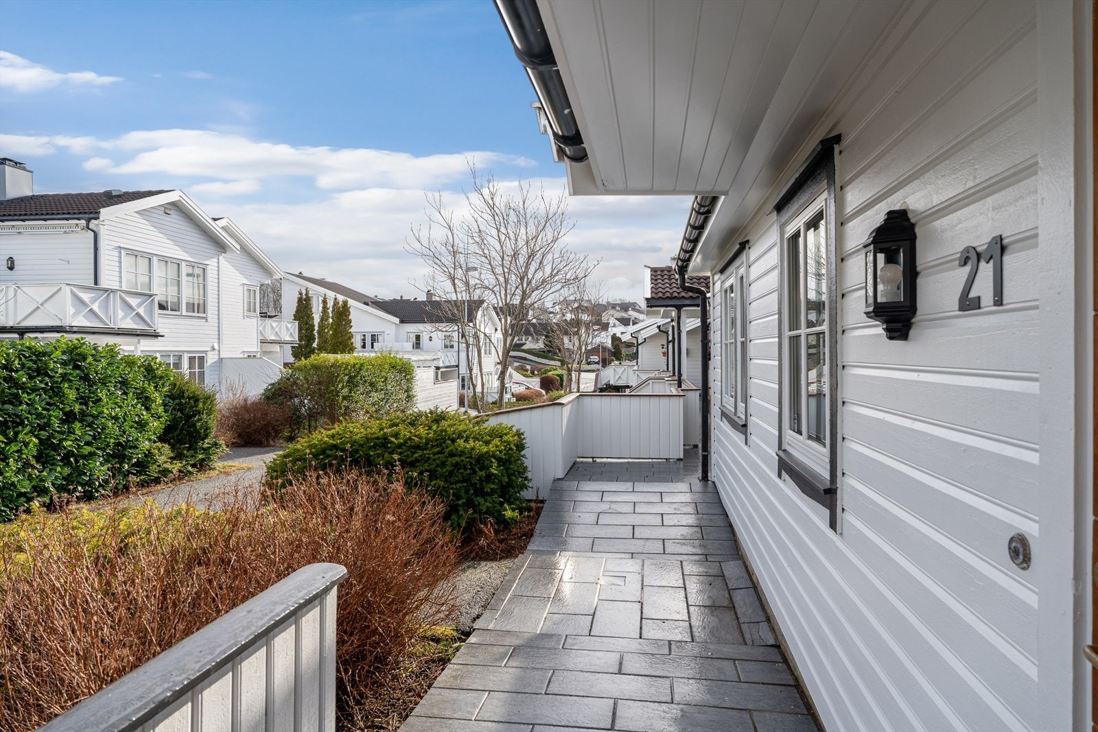 Inngangsparti pent opparbeidet med fliser, gjerde og busker. Galleribilde