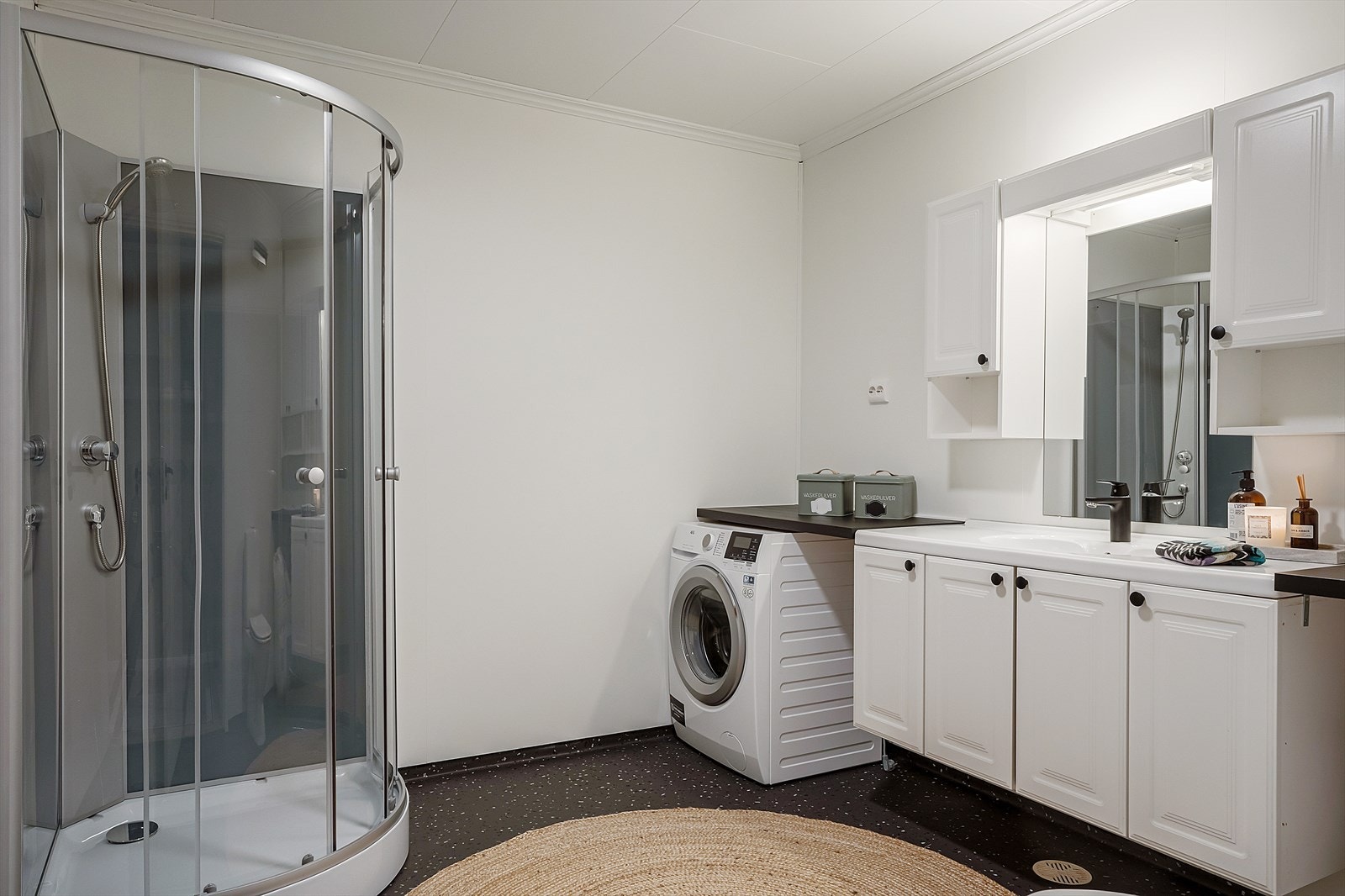 Baderom som inneholder dusjkabinett, toalett, baderomsinnredning og opplegg for vaskemaskin. Galleribilde