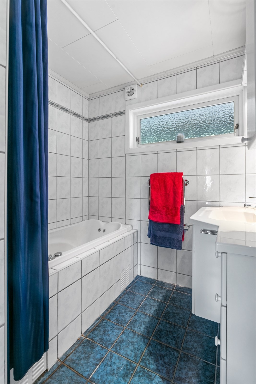 Flislagt bad med gulvvarme, massasjekar, elektrisk håndkletørker og innredning med over- og underskap. Galleribilde