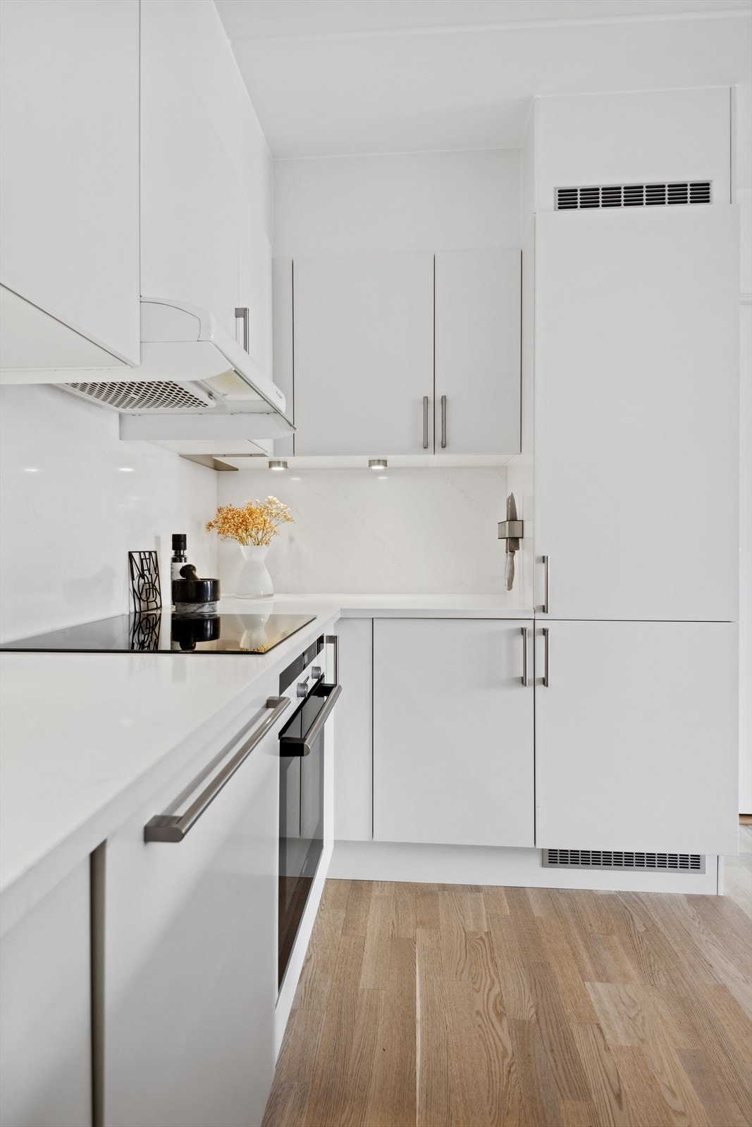 HTH kjøkkeninnredning med lyse matte fronter og skapøy, benkeplater i kompositt, underlimt oppvaskkum, ventilator og integrerte hvitevarer. Galleribilde