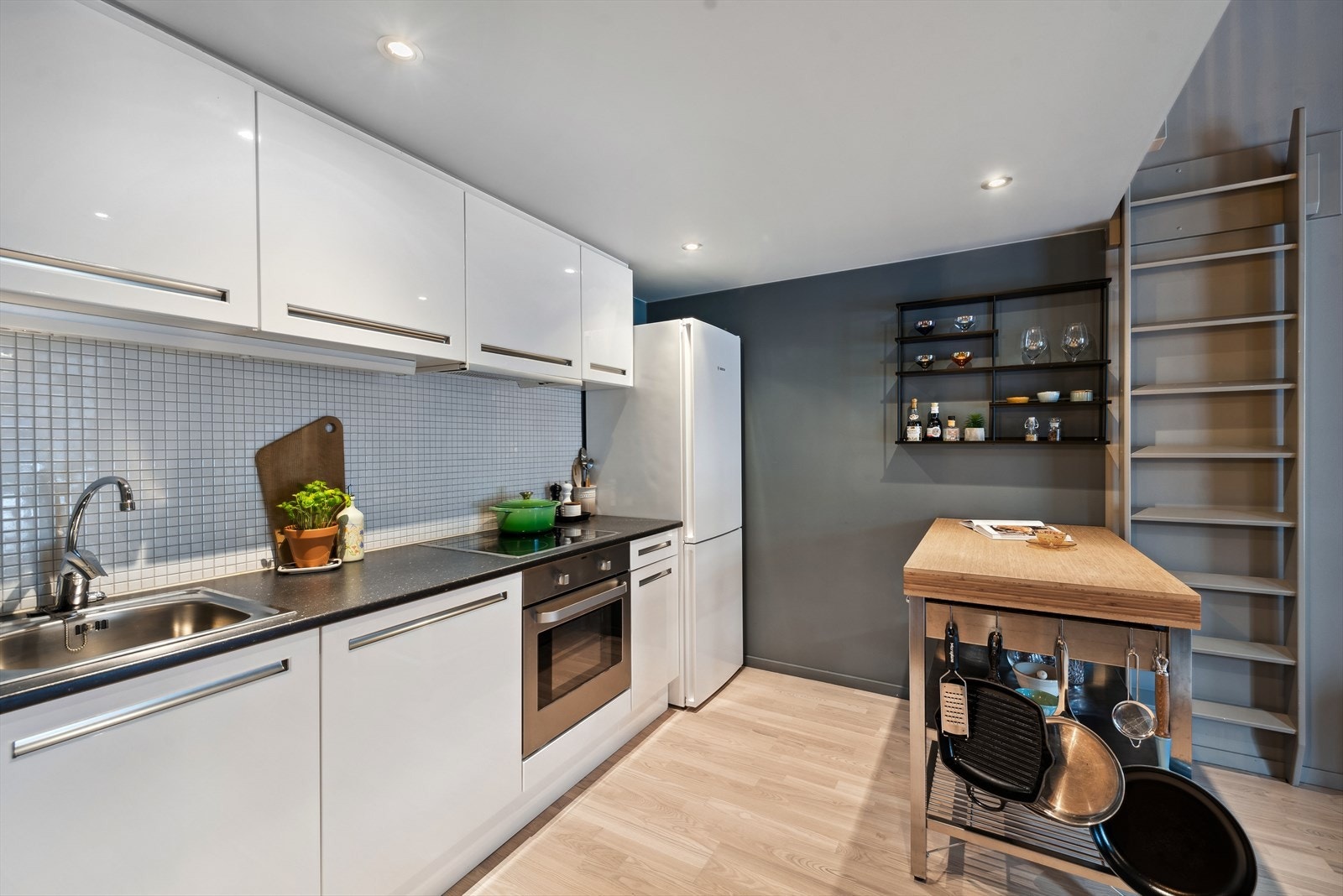 Kjøkkeninnredning med hvite glatte fronter, benkeplate i laminat, rustfri oppvaskkum, ventilator og integrerte hvitevarer. Galleribilde