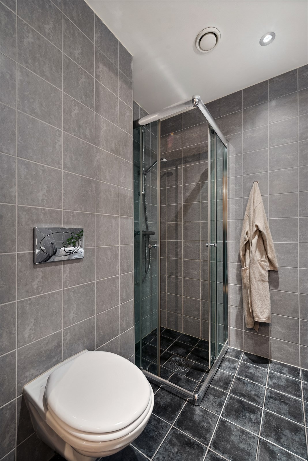 Veggmonterte dusjvegger, dusj direkte på gulv med termostat batteri, veggmontert klosett, servant med skapinnredning og speil med belysning. Galleribilde