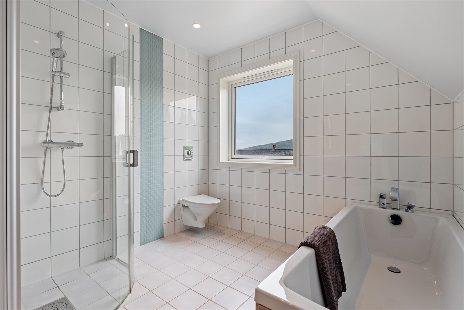 Dobbel heldekkende servant på skuffeseksjon, høyskap, speil med integrert lys, dusjhjørne med buede glassdører, badekar og veggmontert toalett. Galleribilde