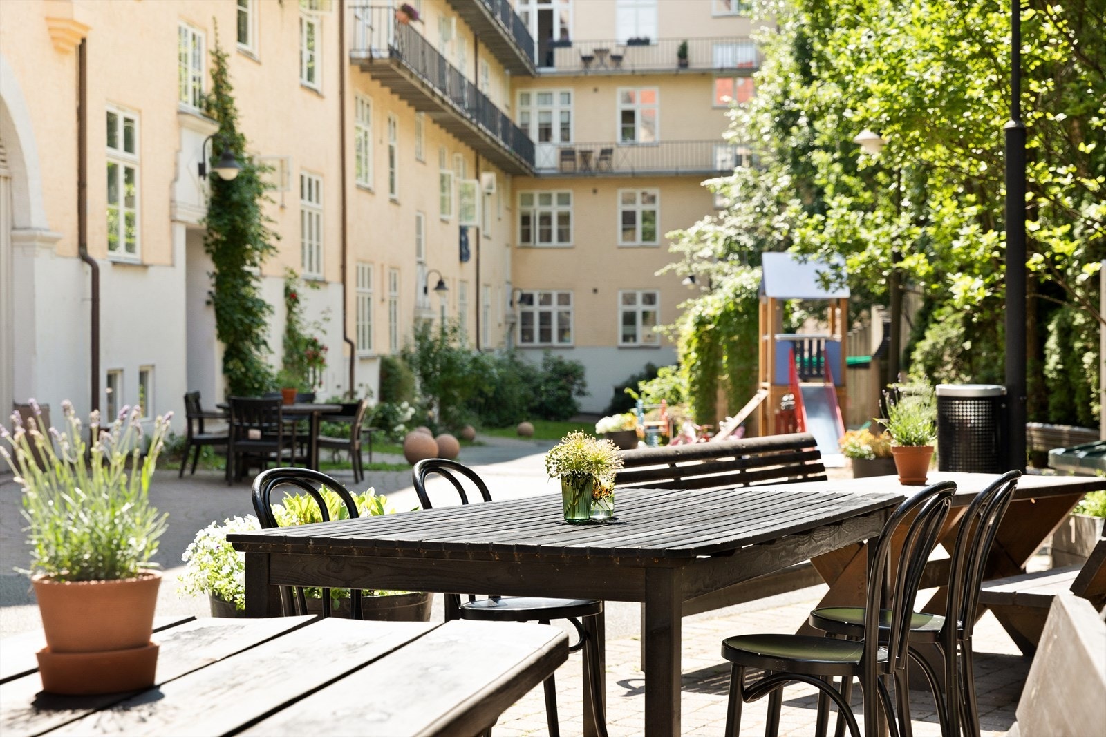 Flere sittegrupper i fellesbakgård med flere plantekasser og grill. Galleribilde