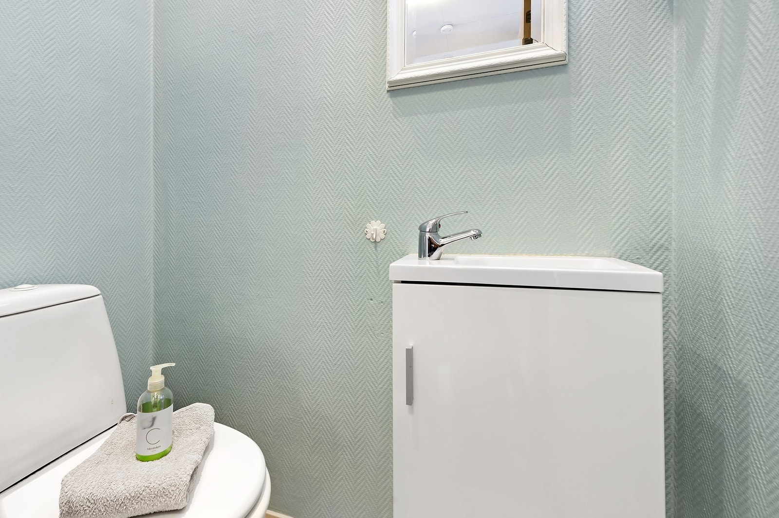 Wc-rom har vinylbelegg på gulv og malt strietapet på vegger. Toalett og nedfelt servant Galleribilde