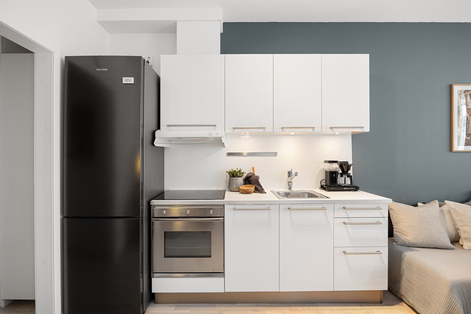 Innredning med glatte, hvite fronter og laminat benkeplate. Det er integrerte hvitevarer med oppvaskmaskin, stekeovn og platetopp Galleribilde