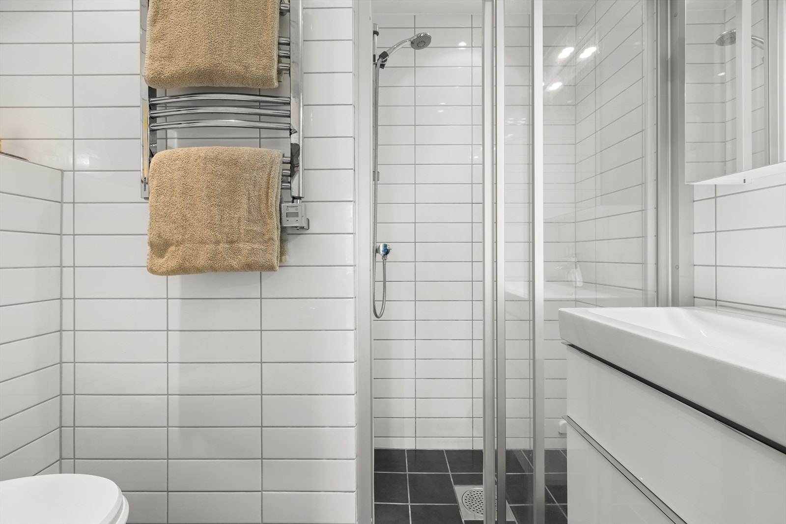 Flislagt baderom bestående av servant med underskuff, vegghengt toalett og dusjhjørne Galleribilde