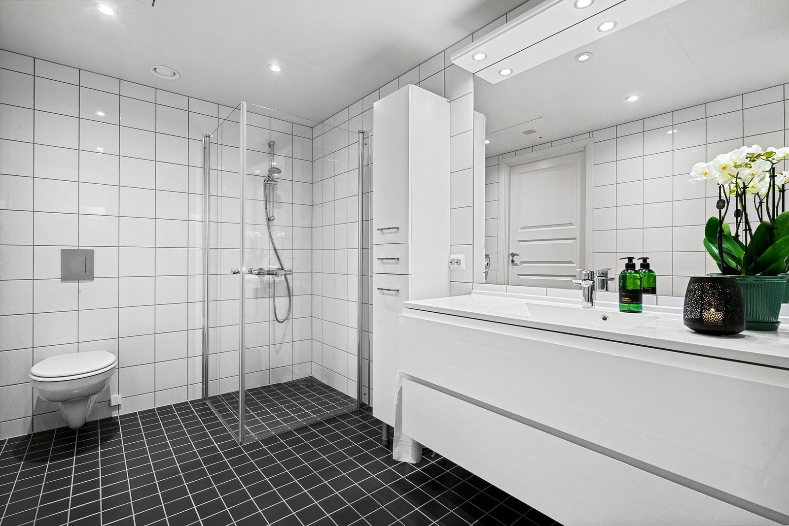 Badet er flislagt med dusjvegger og moderne innredning med overlys over speil Galleribilde