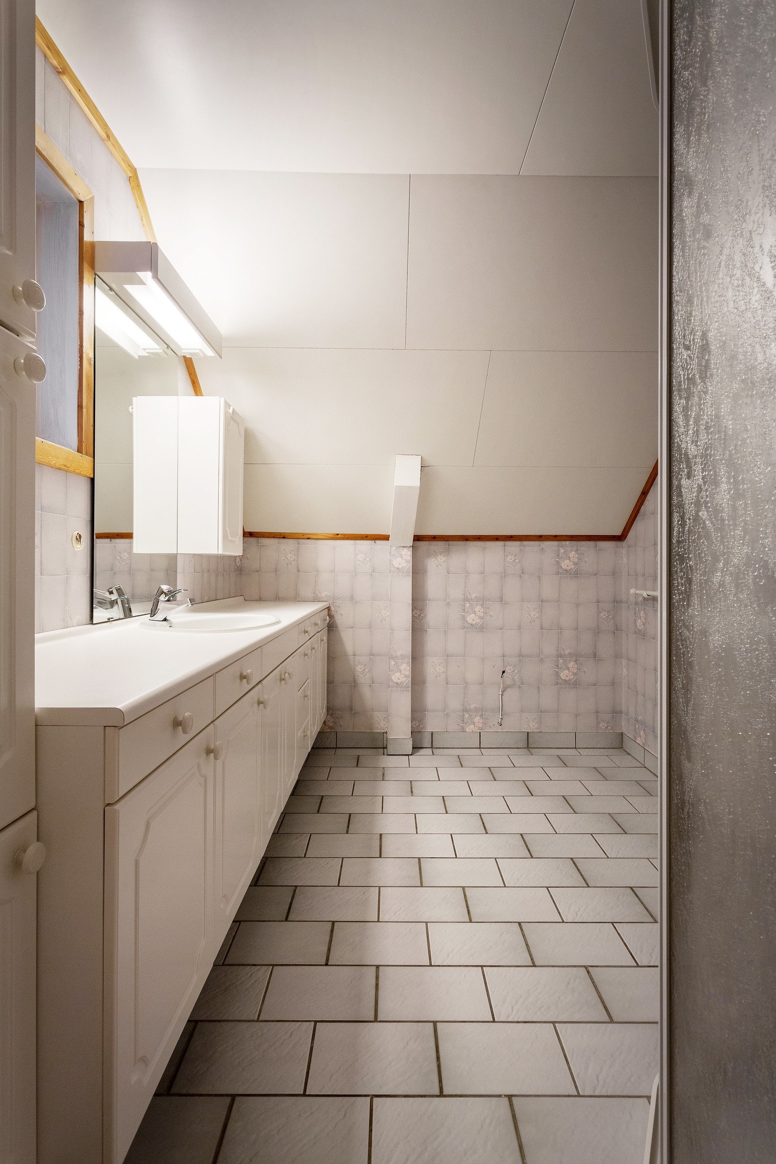 Loftsetasjen har også et eget bad. Dette ble sist renovert ca. 1990 og har standard fra datidens byggeskikk. Flislagte gulv med varmekabler, innredning med vask og dusjnisje med flislagte vegger. Ellers vinyltapet på veggene. Galleribilde