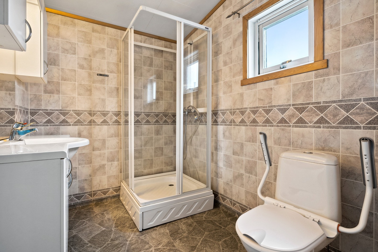 Badet er enkelt innredet med toalett, skapinnredning og dusjkabinett Galleribilde