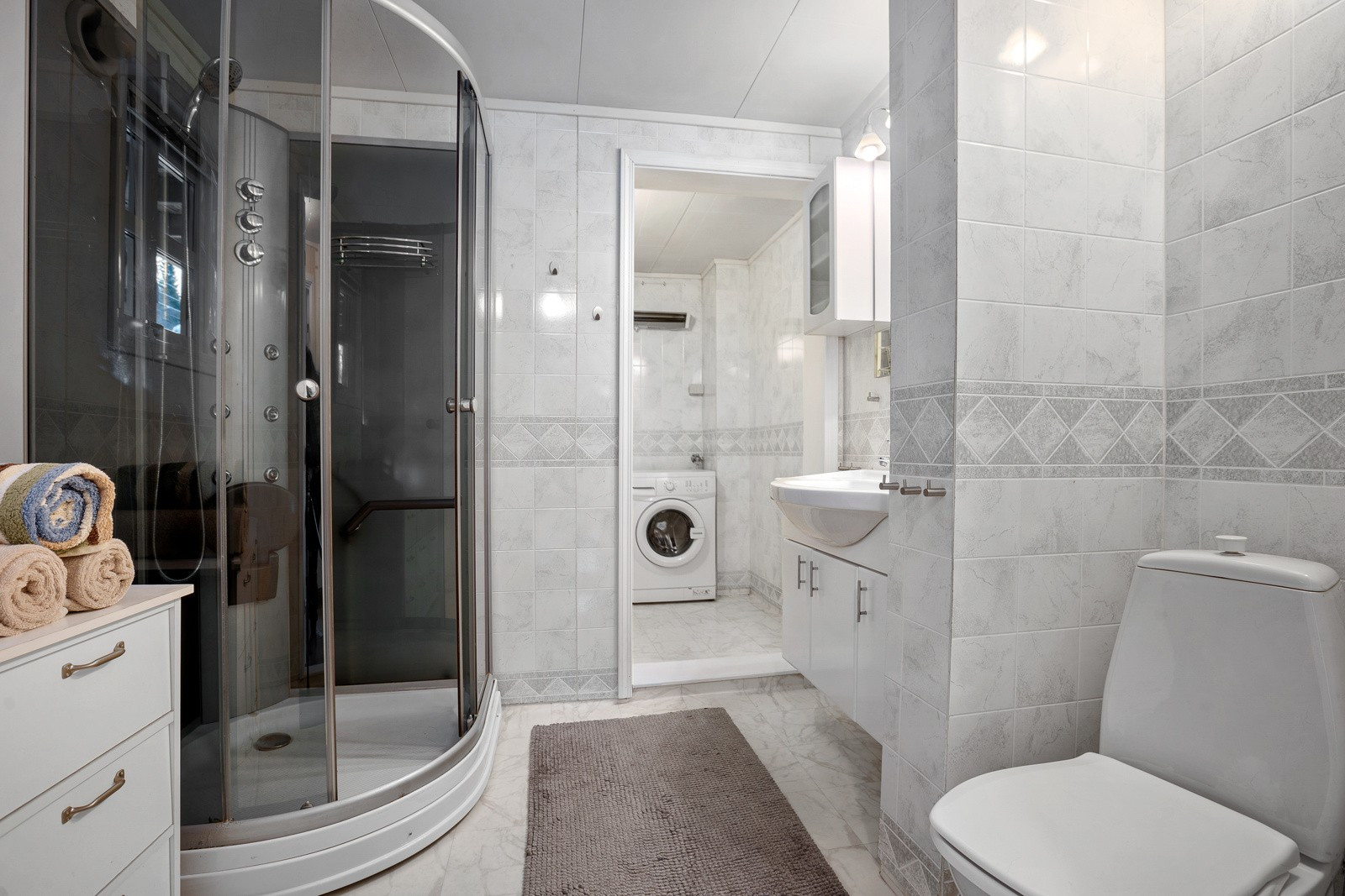 Romslig bad/vaskerom med stort dusjkabinett, wc, servant med oppbevaringsplass og god plass for vaskemaskin/tørketrommel.