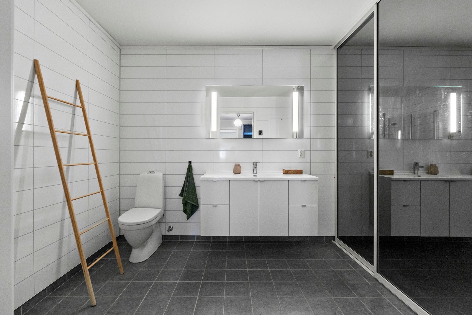 Kombinert bad og vaskerom i underetasjen - vaskemaskin og varmtvannstank er praktisk plassert bak skyvedørsgarderoben Galleribilde