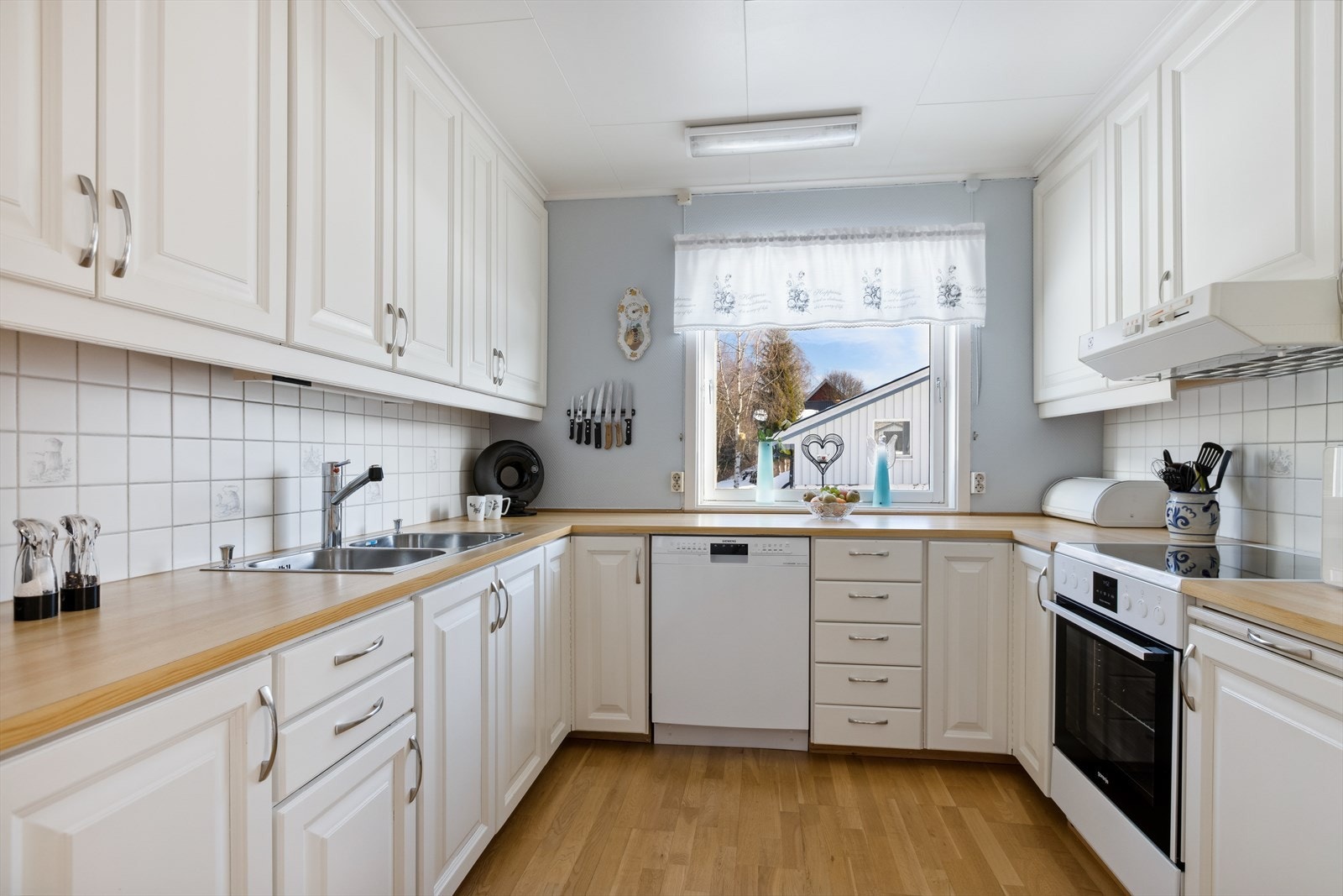 Hesteskoformet takhøy heltre kjøkkeninnredning med profilerte, malte speilfronter og laminat benkeplate. Galleribilde