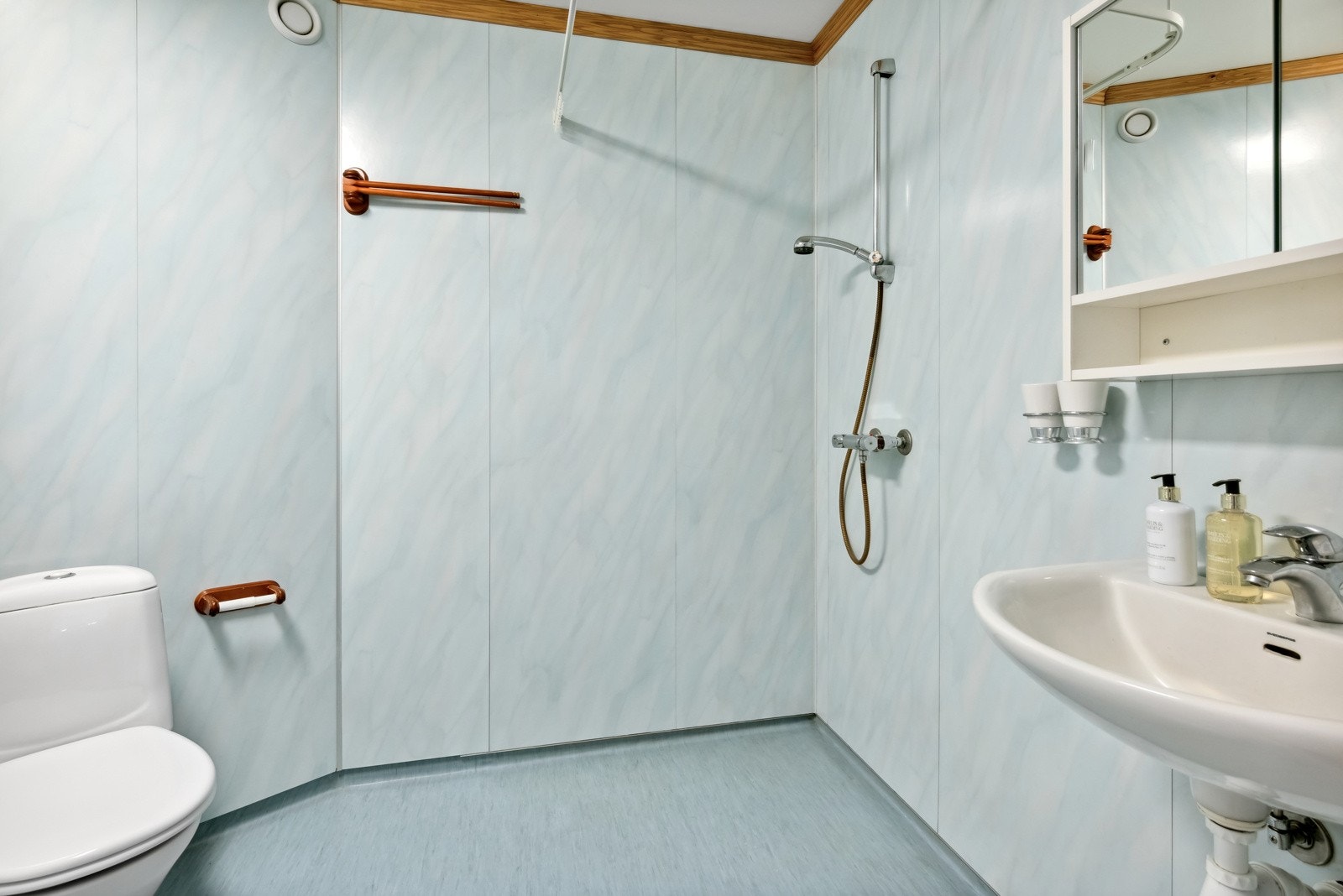 Badet inneholder gulvstående toalett, servant m/speilskap og lysarmatur, et høyskap og åpen dusj m/dusjgarnityr. Galleribilde