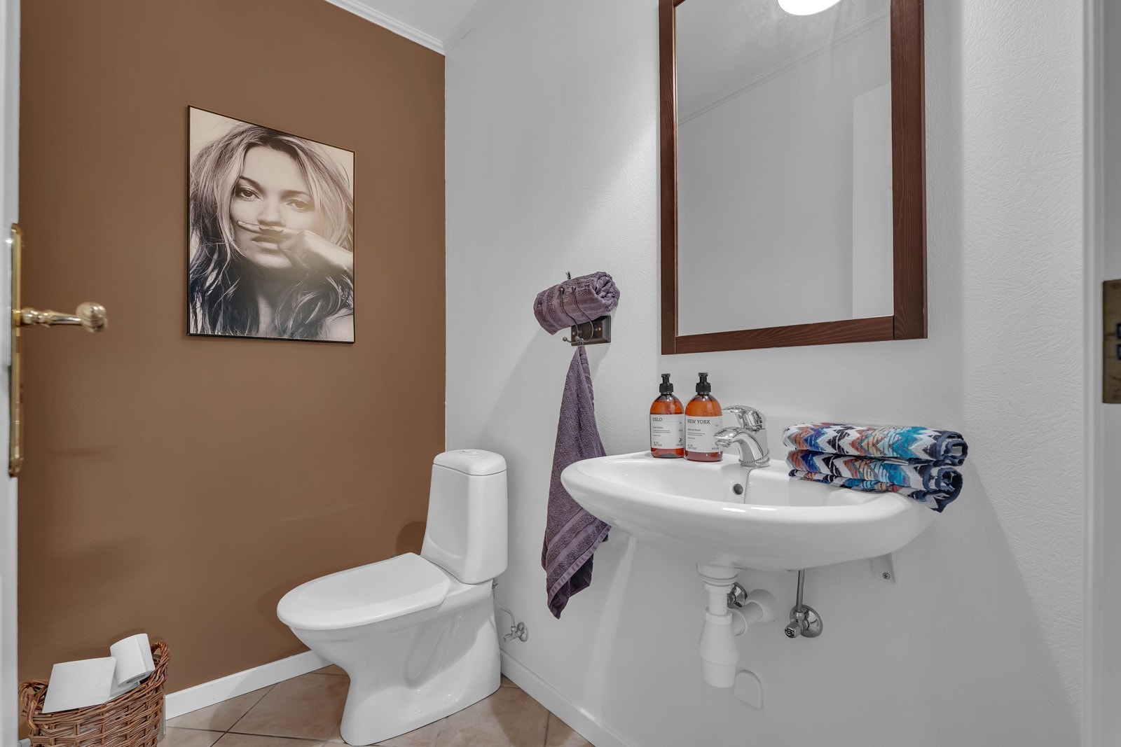 WC-en i 1.etasje ligger i tilknytning til hallen. Rommet har flislagte gulv, med samme fliser som i hallen. Veggene er malt hvite, med en kontrastvegg i dus brun. WC-en har servant og gulvstående klosett. Galleribilde