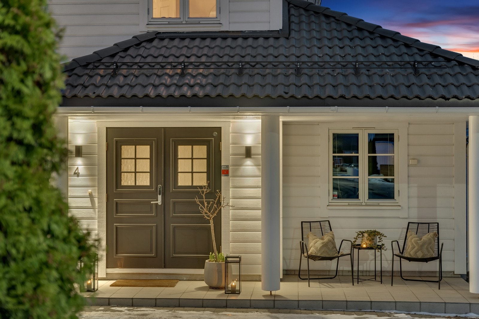 Boligen har et overbygd inngangsparti med doble dører, som er med på å gi huset en elegant stil. Under det overbygde inngangspartiet er det passende å innrede med en liten sittegruppe, hvor morgenkaffen kan nytes i morgensolen. Galleribilde