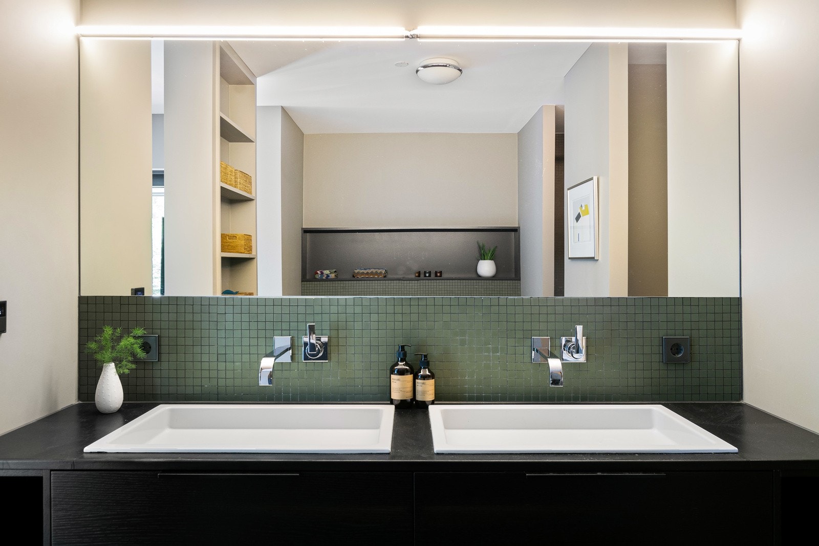 Badet har bredt speil med ledbelysning, to integrerte blandebatterier og to servanter nedfelt i skapinnredning med mørke fronter i eikestruktur. Galleribilde