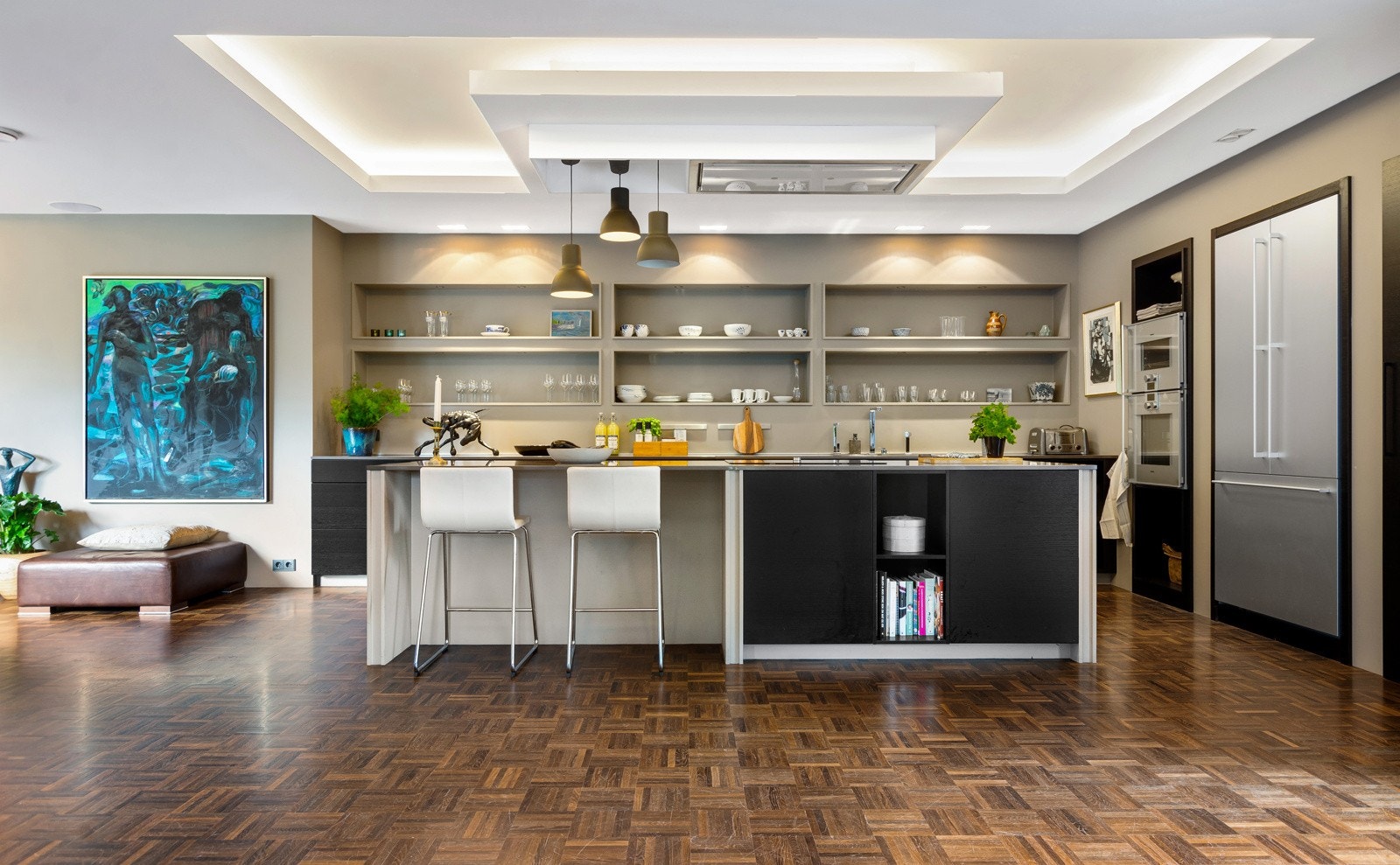 Kjøkkeninnredningen har fronter i mørkbeiset eikestruktur og seks hyller innfelt i veggen over benkeskapene. Benkeplater i stein med underlimt oppvaskkum understreker den påkostede standarden - og øya er selvfølgelig utført i samme materiale. Galleribilde