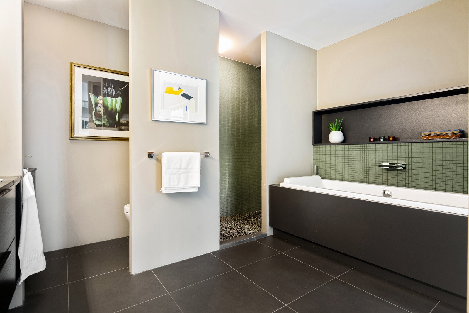 Her bys det på innebygget badekar med integrert dusjløsning, armatur med fossefall og en bred hylle over karet. I tillegg er det en åpen dusjnisje med plassbygget hylle. Det er også egen sone med vegghengt toalett. Galleribilde