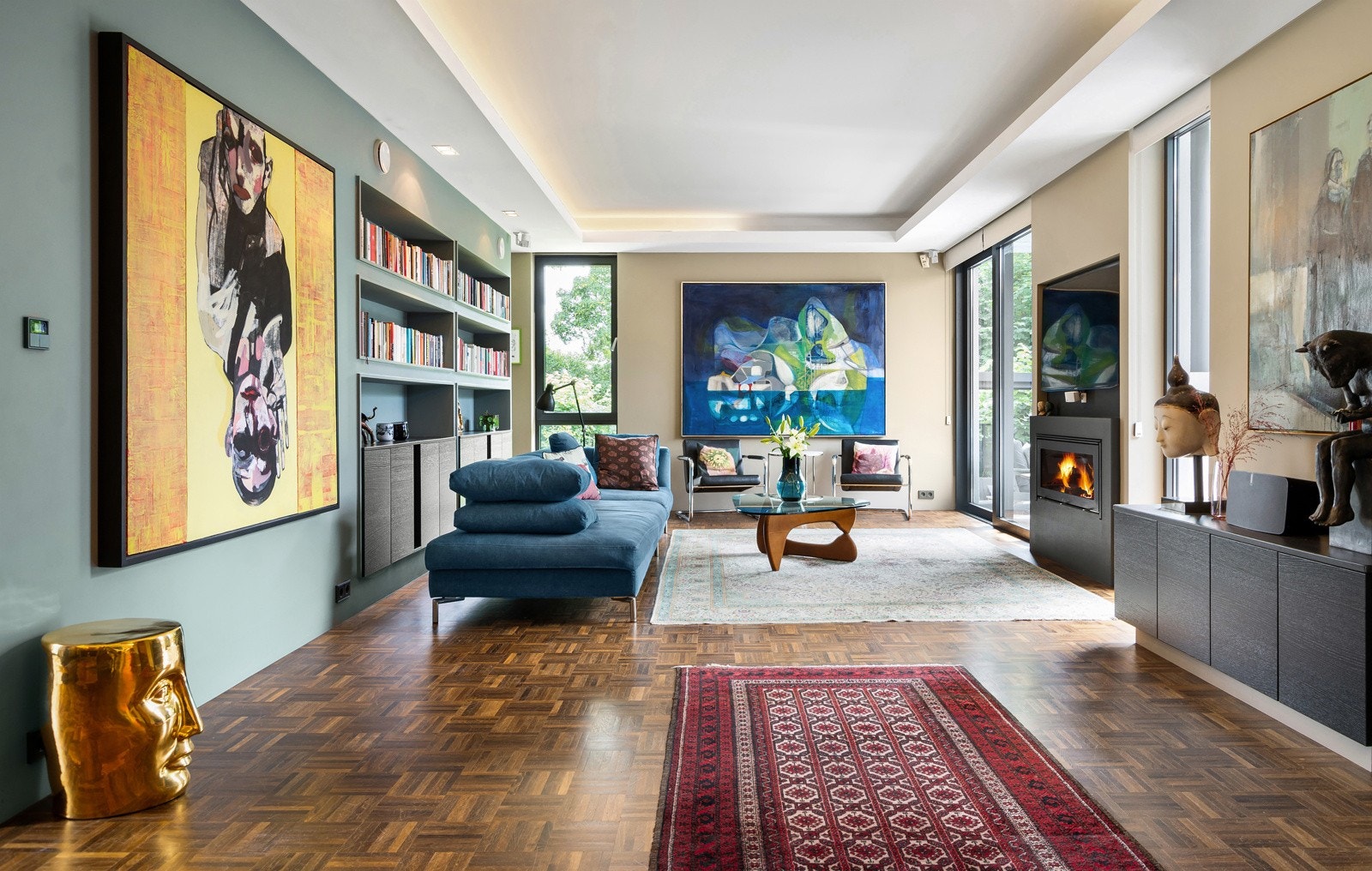 Stuen har en bred vegg med fastmonterte bokhyller og plassbygde skap. En stilfull innsatspeis skaper varme og hygge på kjøligere dager, mens nedforede felt i himlingen med skjult belysning setter prikken over i-en. Galleribilde