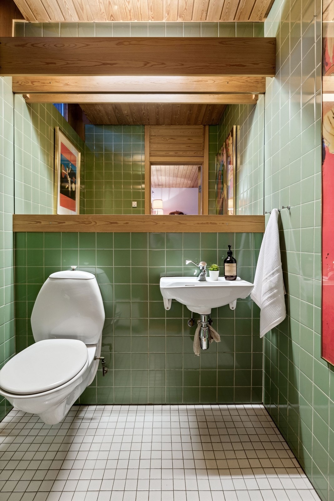 Toalettrom med flis på gulv og vegger. Panel i himling. Rommet er innredet med vegghengt toalett og servant. Galleribilde