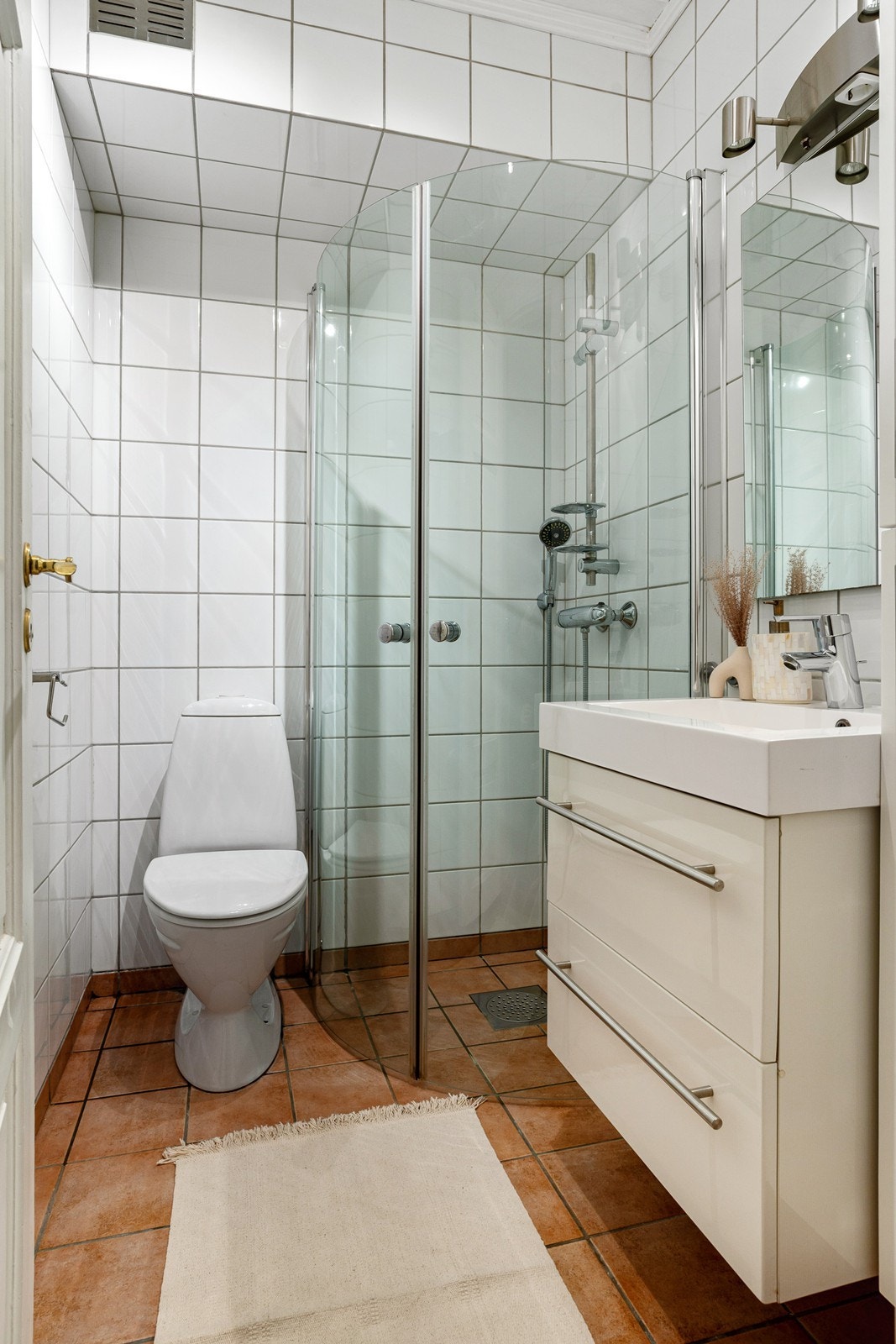 Lyst baderom bestående av servant med skuffer, dusjhjørne med foldedører i glass og frittstående wc. Galleribilde