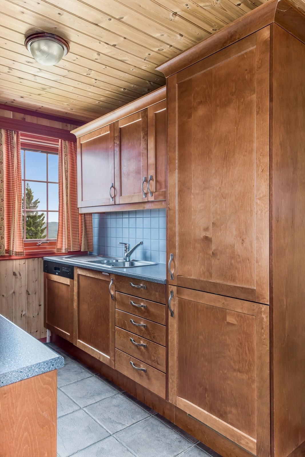 Innredning med profilerte dører, fliser mellom over- og underskap og stålkum med ett-greps kran. Fint med lys og utsikt også fra kjøkkenkroken Galleribilde