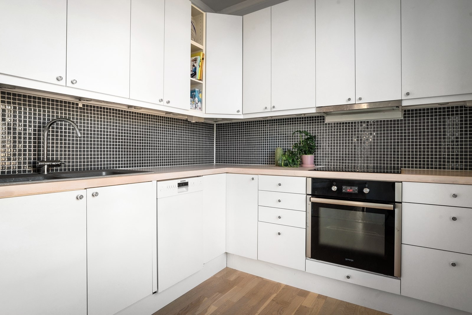 Kjøkkeninnredning fra 2012 bestående av slette lyse fronter, heltre benkeplate med nedfelt oppvaskkum og skyllekum. Fliser mellom overskap og benk Galleribilde
