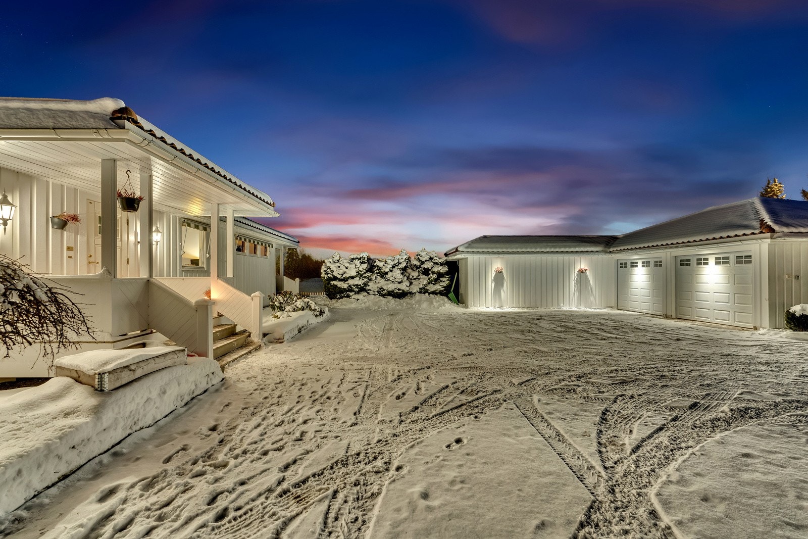 På forsiden av boligen er gårdsplassen belagt med belegningsstein mellom hus og den doble garasjen. Boligen har et overbygd inngangsparti med trapp opp til inngangsdøren. Galleribilde