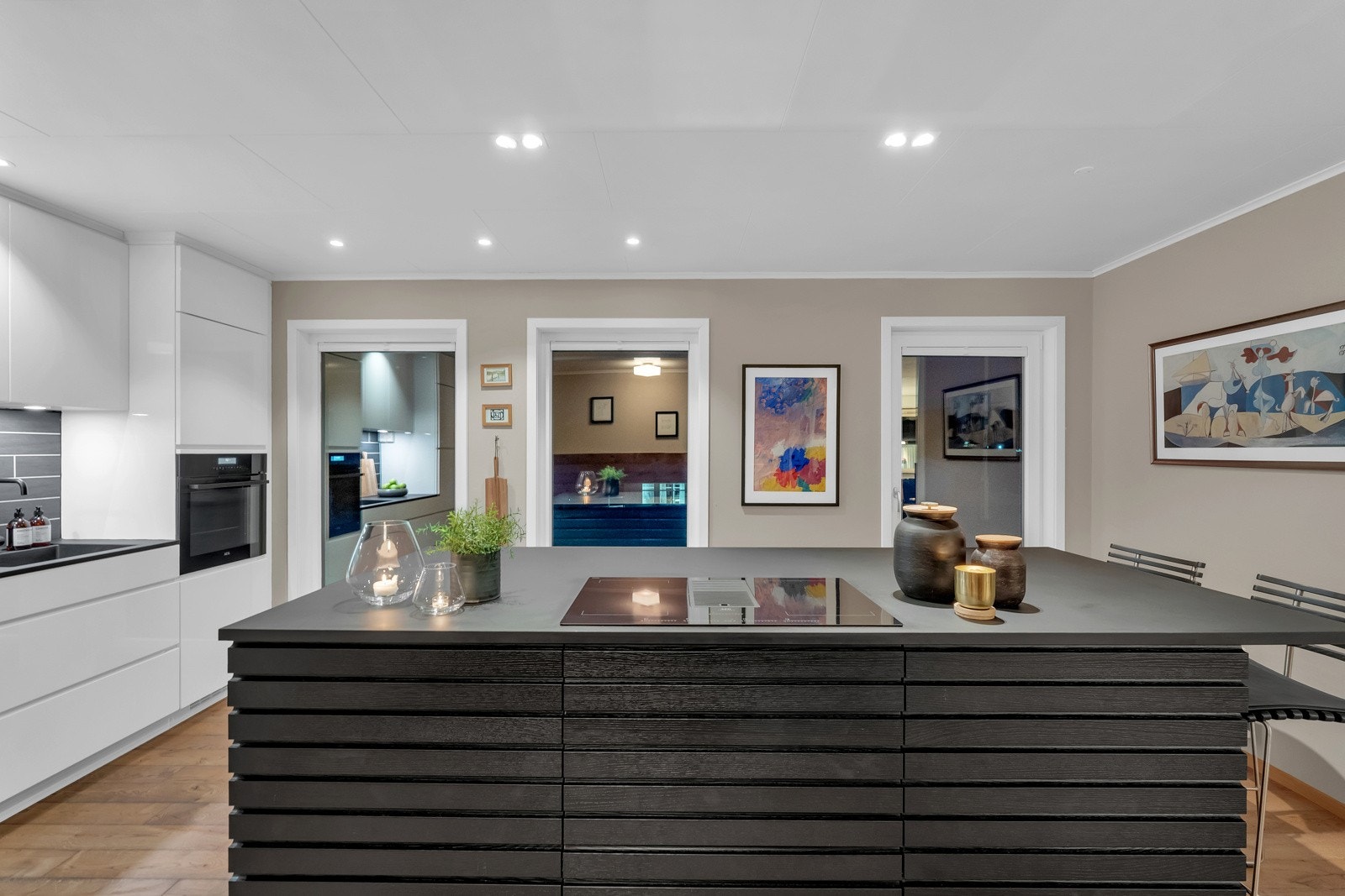 Midt i rommet er det plassert en stor, flott kjøkkenøy. Denne er i en mørk farge og tar igjen fargen i de mørke flisene over benkeskapene på kjøkkenet. Galleribilde