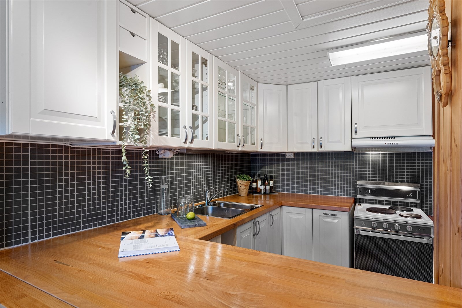 Pen kjøkkeninnredning med komfyr, kjøl/frys og en liten oppvaskmaskin. Galleribilde