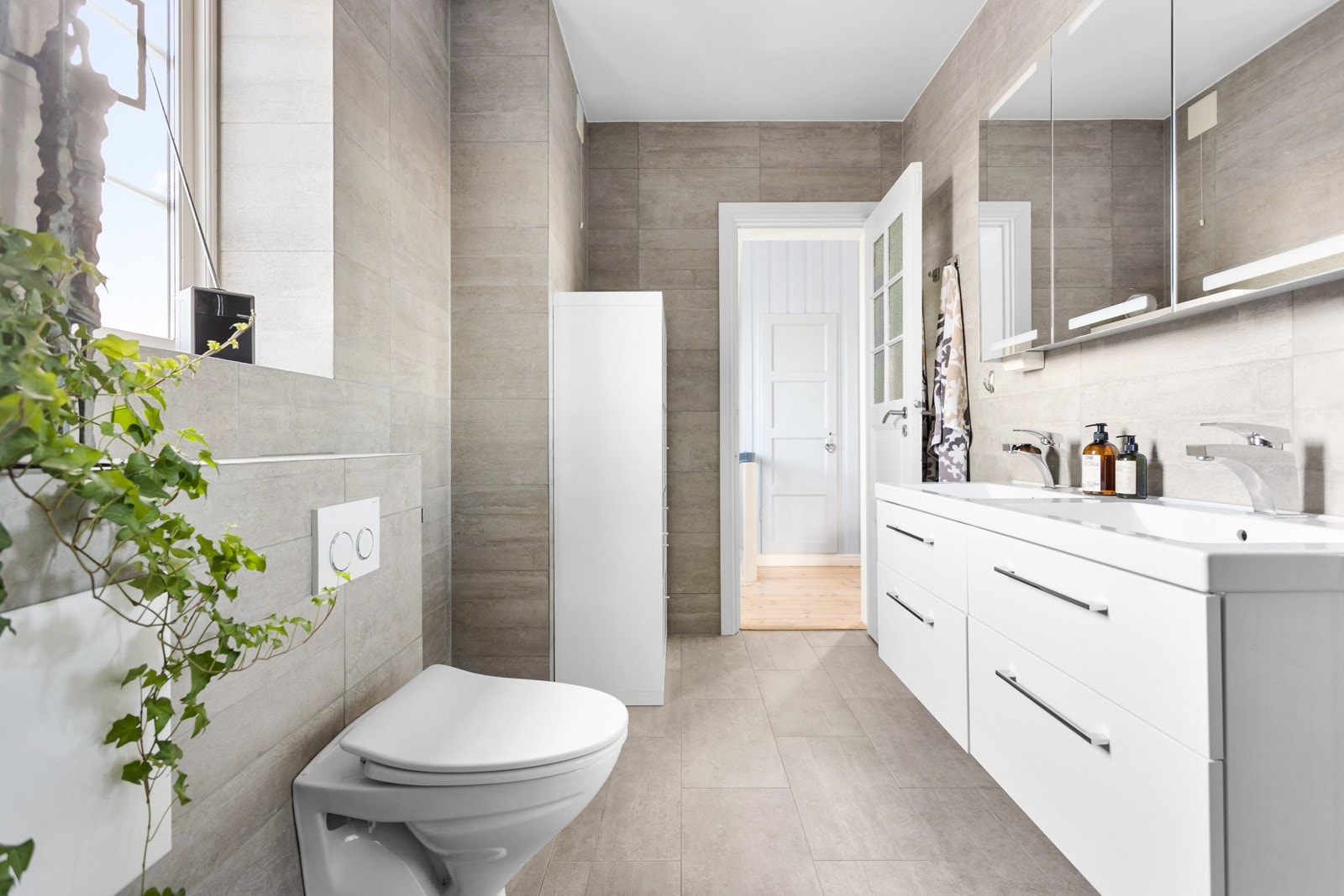 Pent og tidsriktig baderom fra 2013. Badet er utstyrt med vegghengt wc, to servanter med skuffer under og dusj i hjørne med glassdør/vegg. Galleribilde